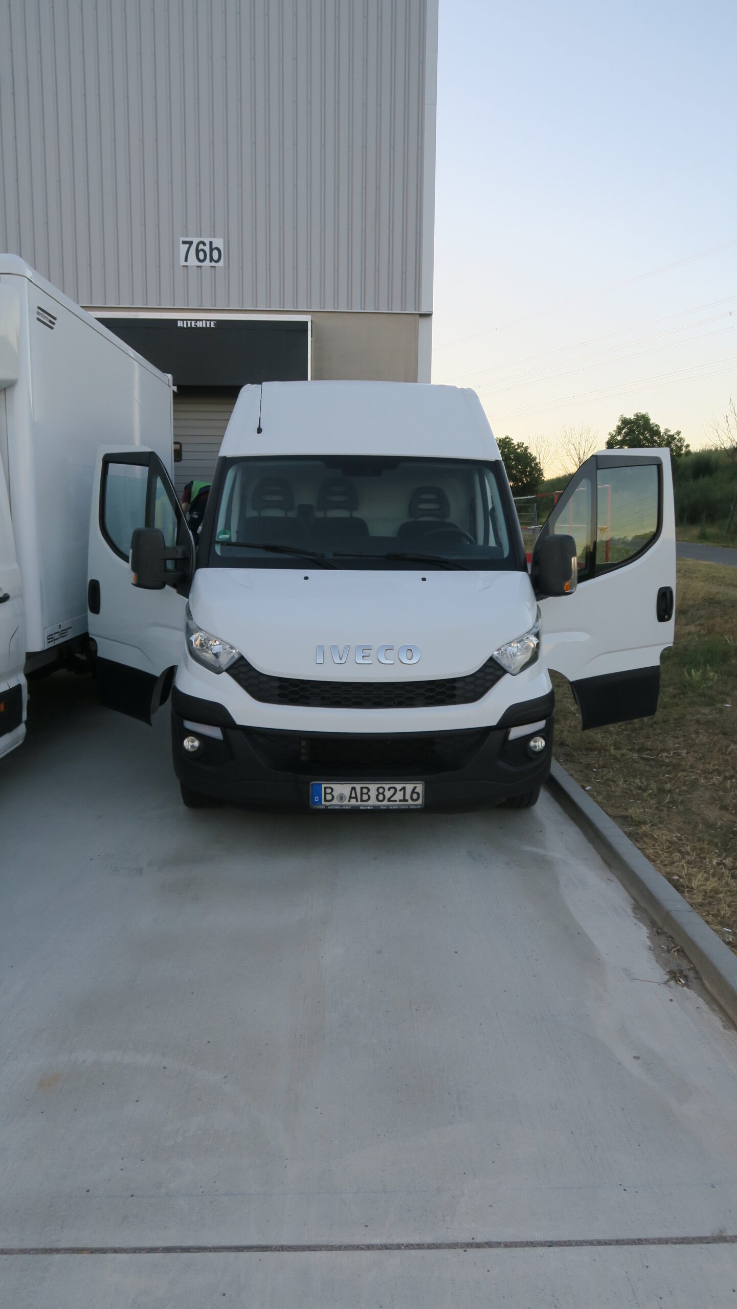 Weißer Lieferwagen mit geöffneten Türen vor Lagerhalle, Kennzeichen aus Berlin.